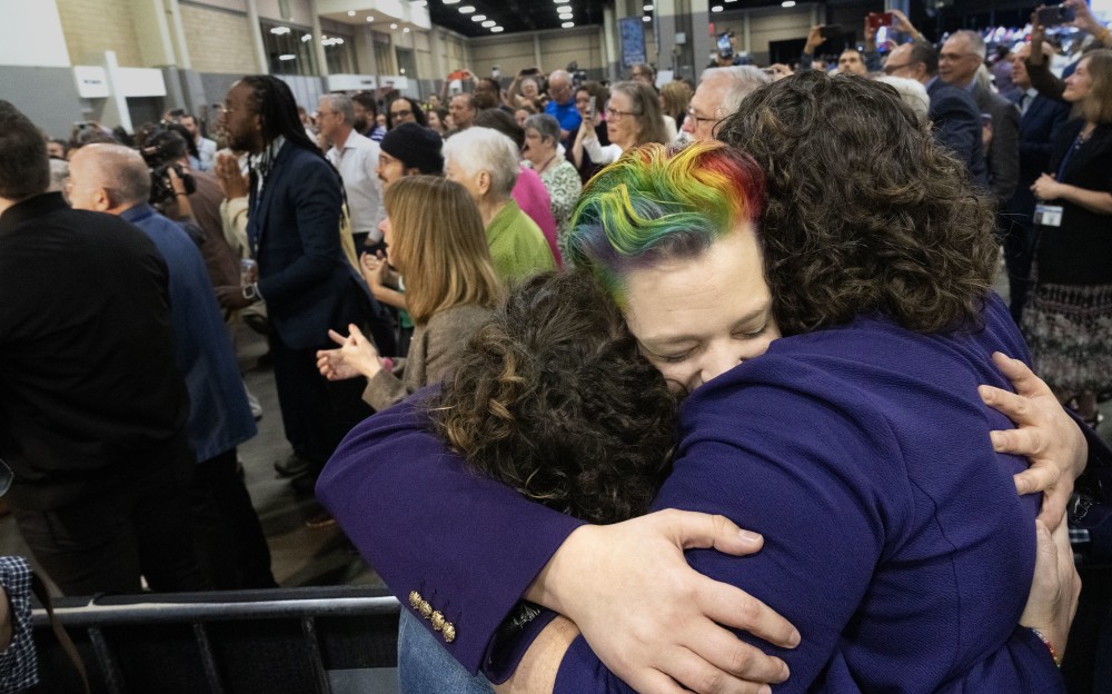 Three people hugging. One of the people has rainbow colored hair.