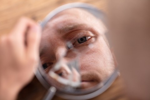 a man looks down into a mirror at his own reflection